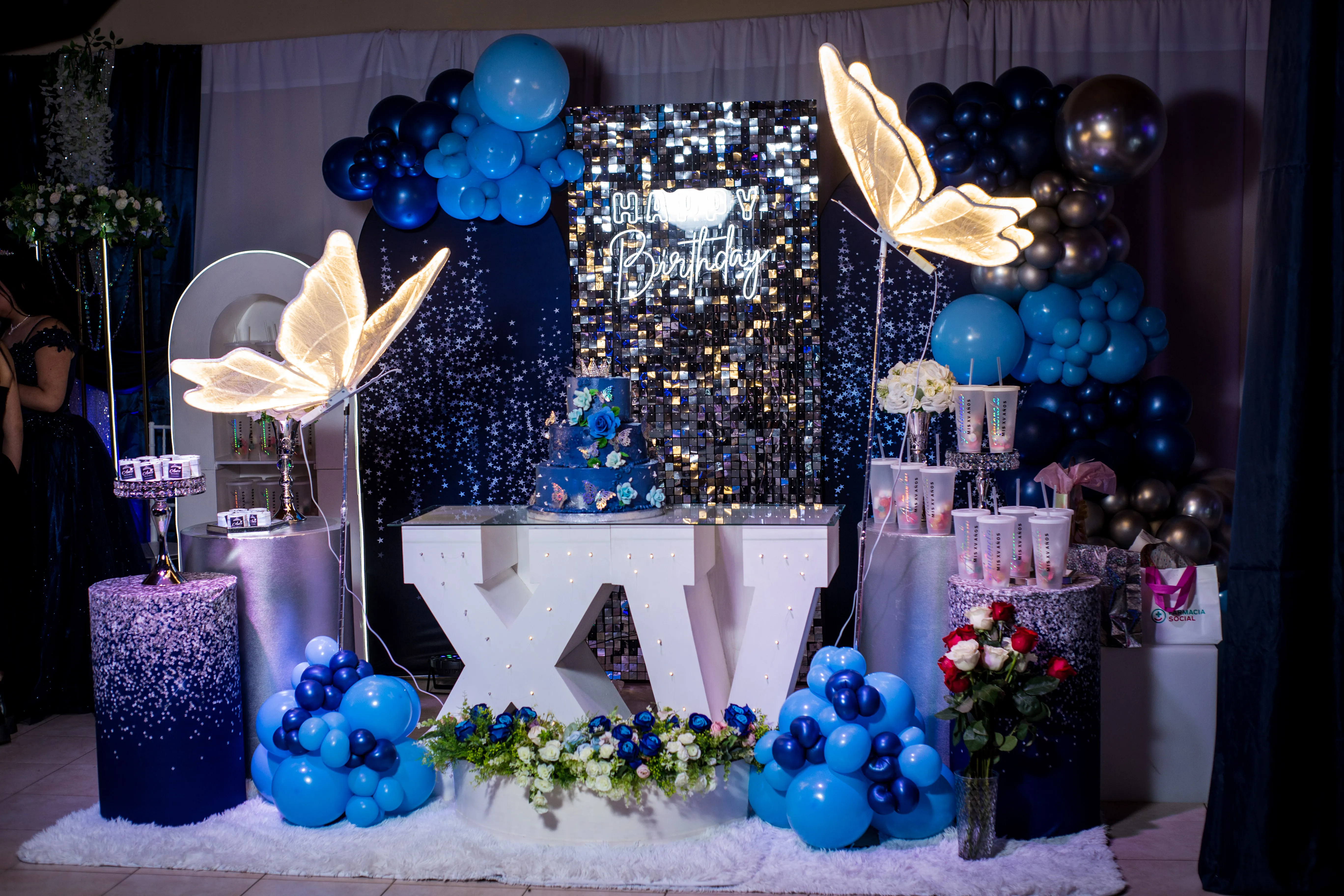 Mesa principal en azul y plata con torta de tres pisos y luces de mariposas para una fiesta de 15