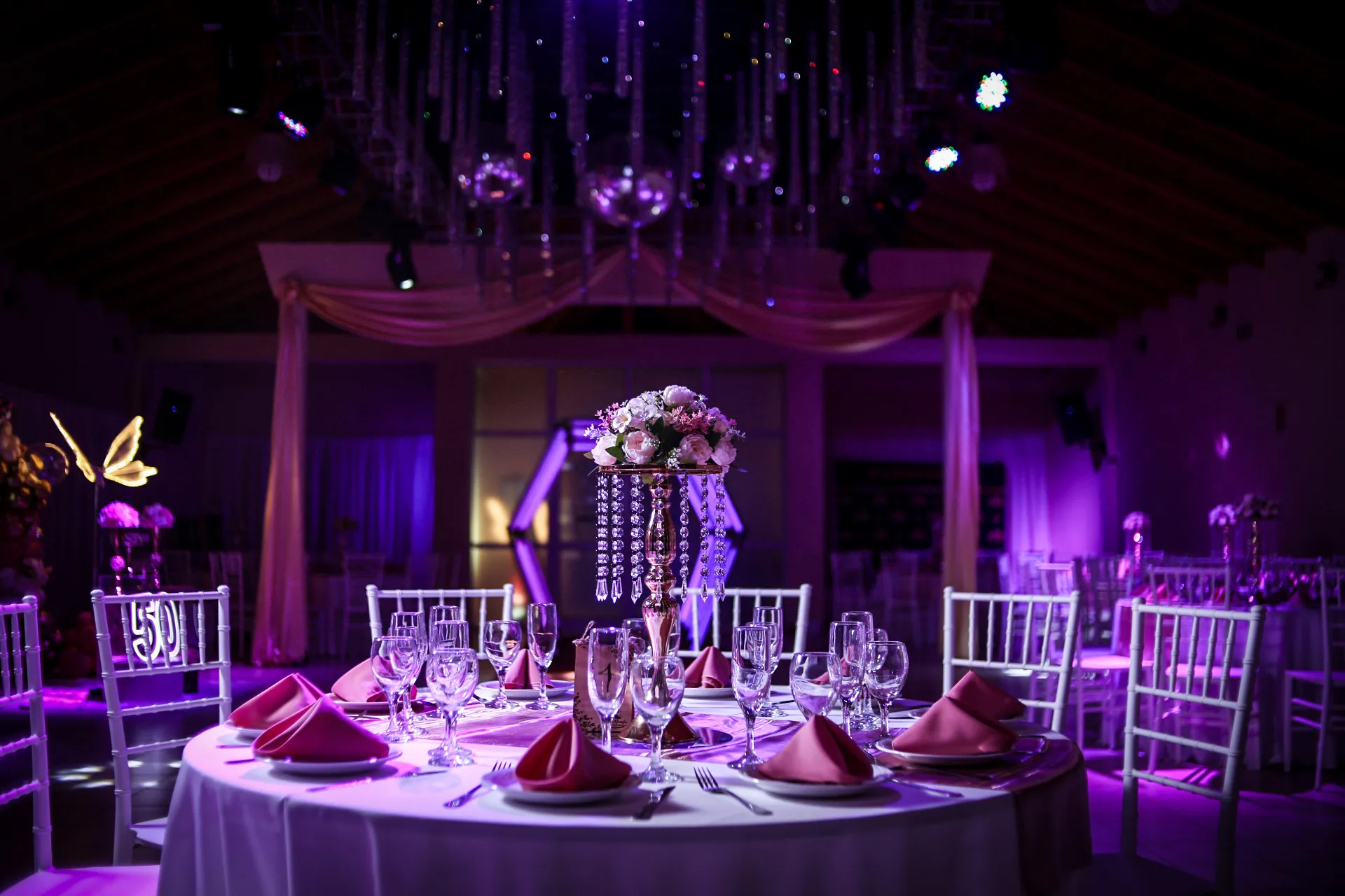 Mesa elegante con centro de cristal y servilletas rosas para un cumpleaños de 50