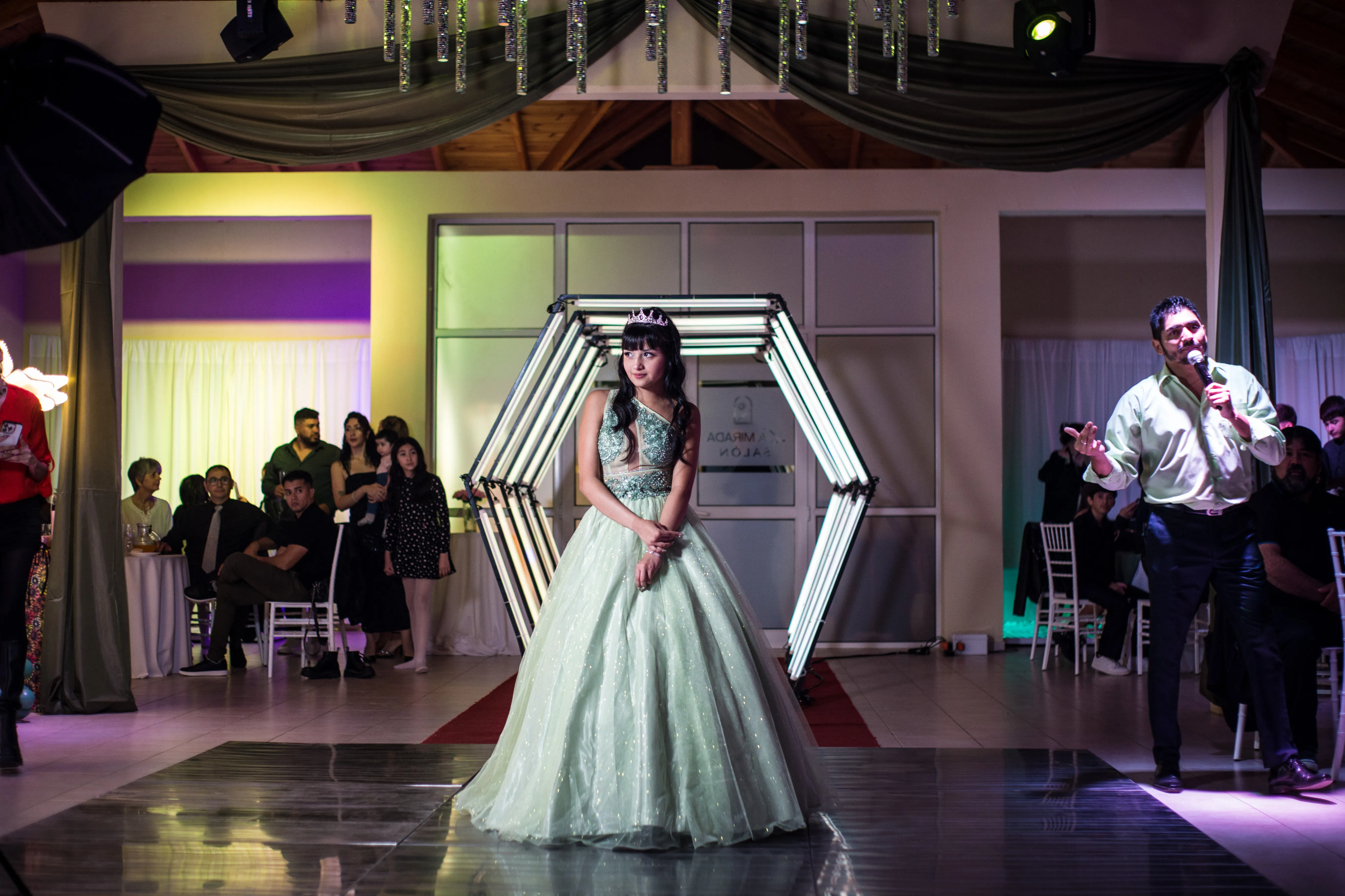 Quinceañera de pie frente al arco hexagonal iluminado antes de su presentación