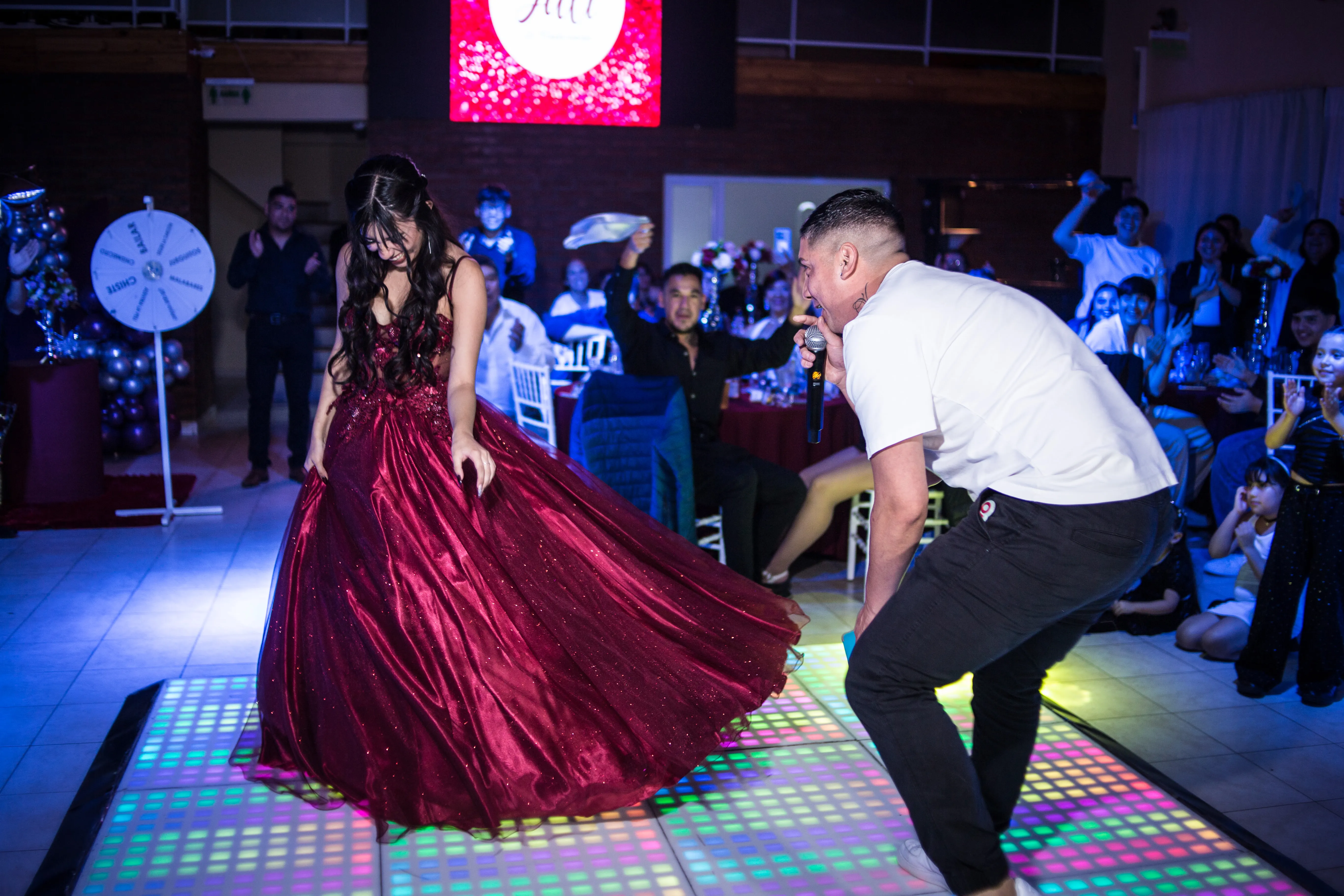 Quinceañera luciendo su vestido bordó mientras baila con el animador de la fiesta