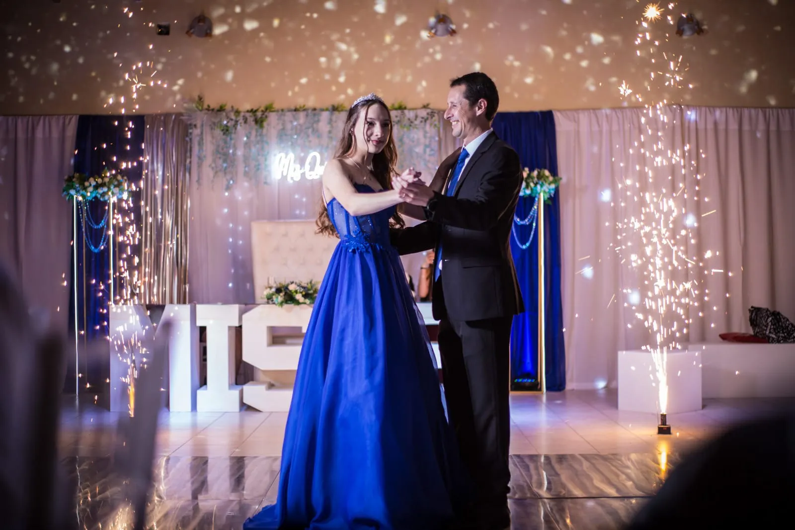 Quinceañera bailando el vals con su papá, con luces de bengala de fondo